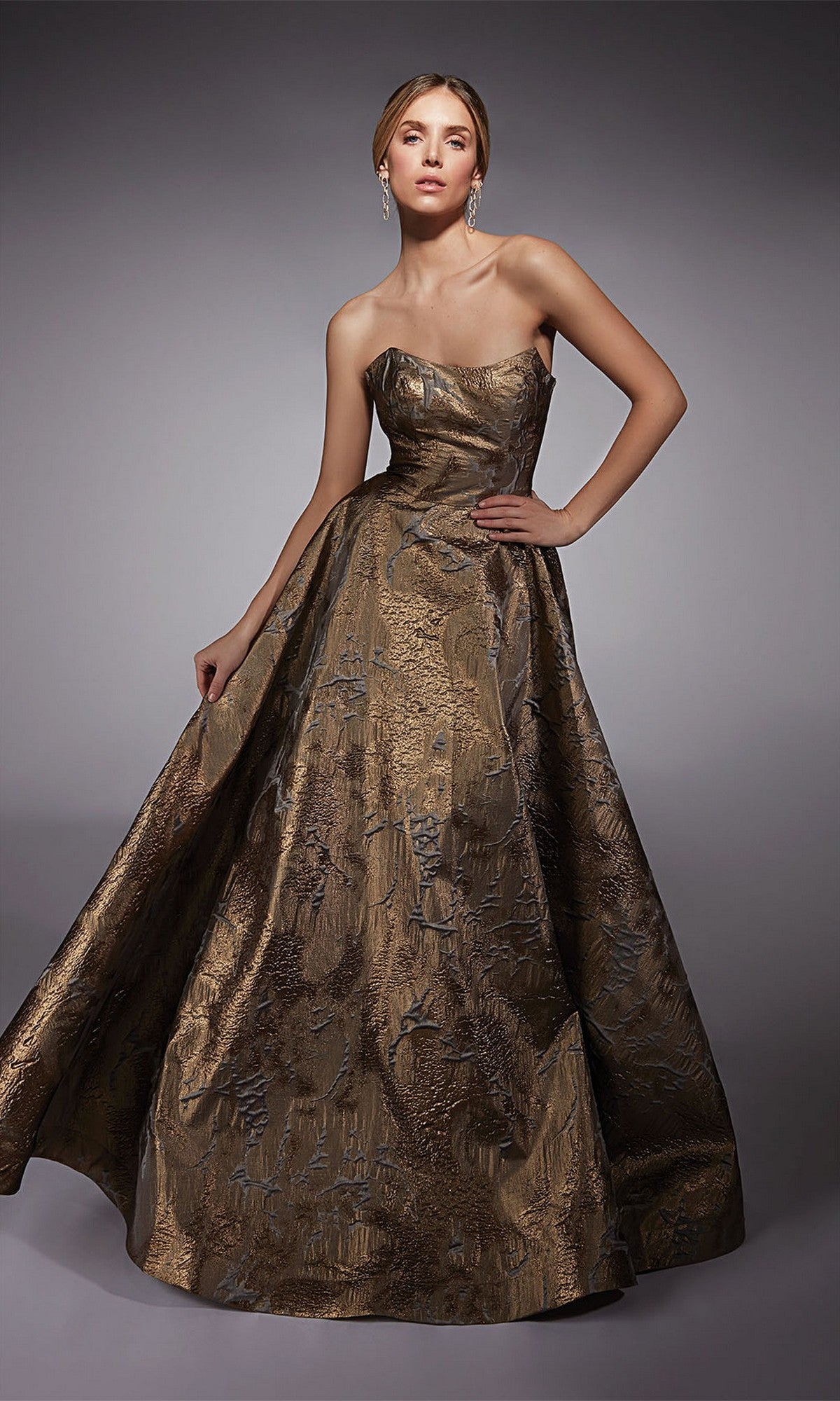 A woman models the Alyce 27760 long formal dress—strapless, featuring metallic gold and bronze jacquard—against a plain gray background.